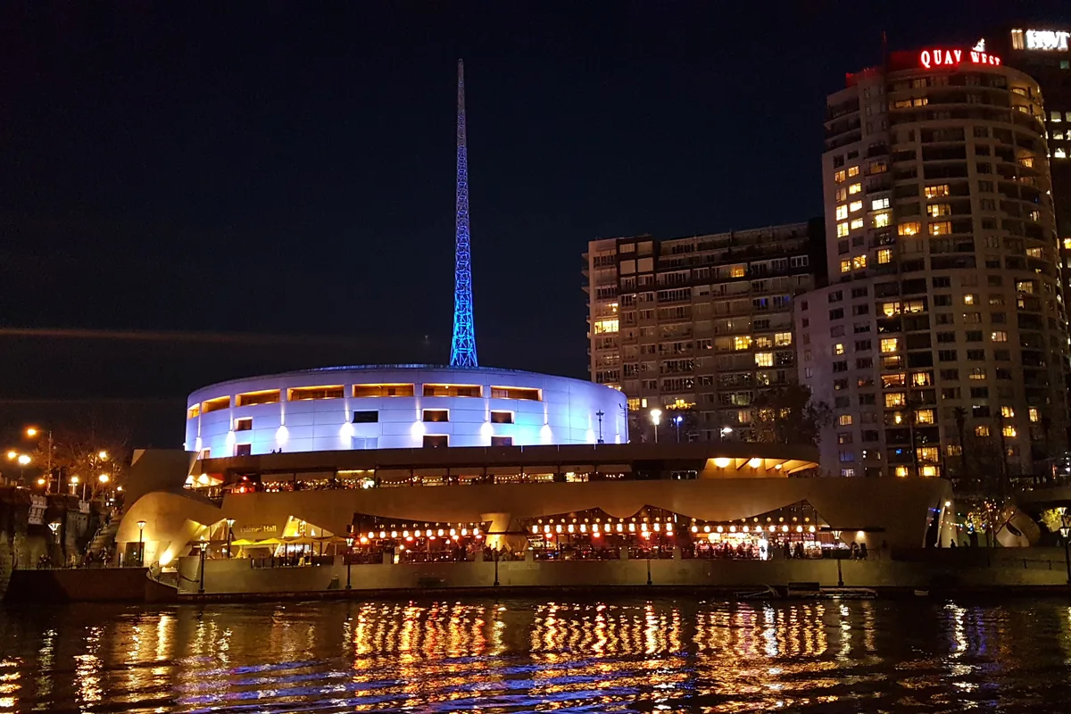 La flèche illuminée et le dôme blanc de l'Arts Centre Melbourne, de l'autre côté de la Yarra, la nuit.