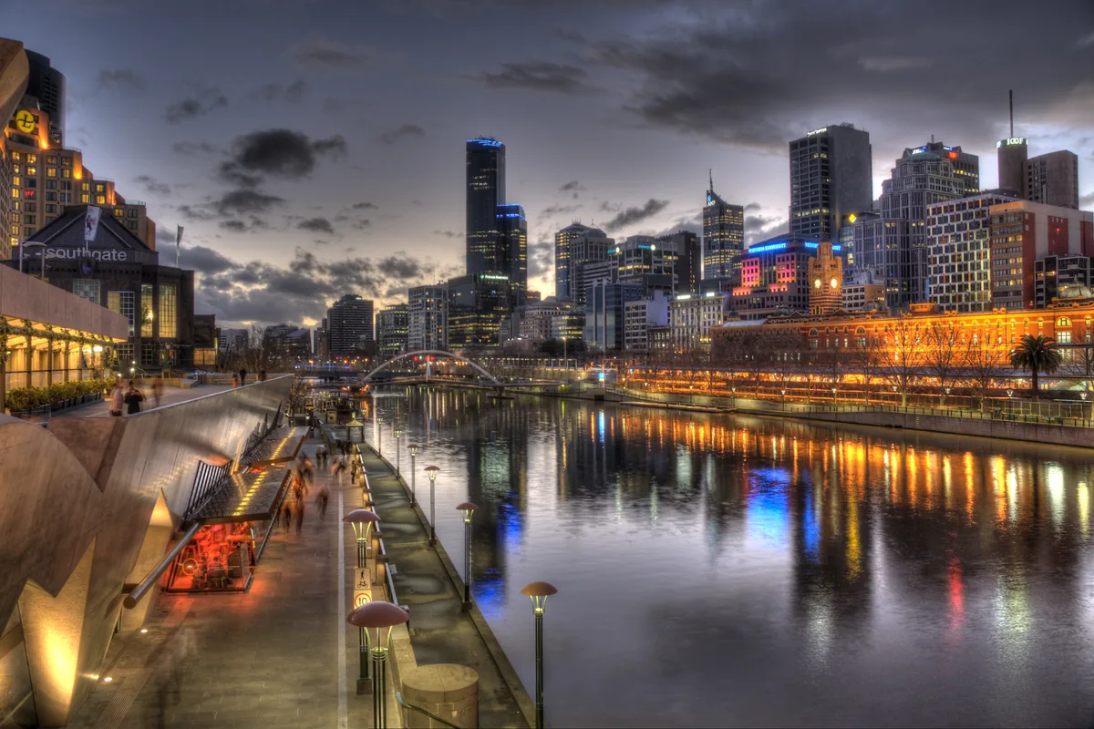 La promenade de Southbank au crépuscule, avec sa rangée de restaurants illuminés et les gratte-ciel de la ville se dressant de l'autre côté du fleuve.