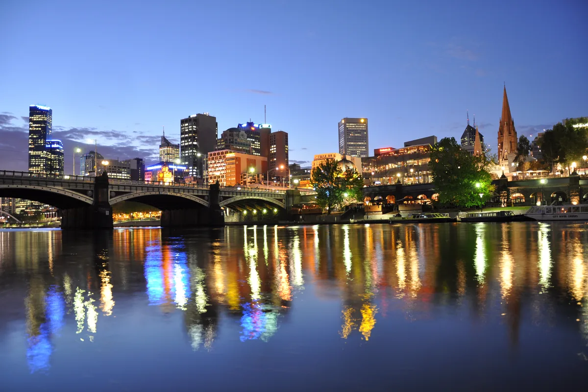 Princes Bridge, stanica Flinders Street, Federation Square a veže katedrály sv. Pavla pozdĺž rieky Yarra za súmraku, s odrazmi svetiel na hladine rieky