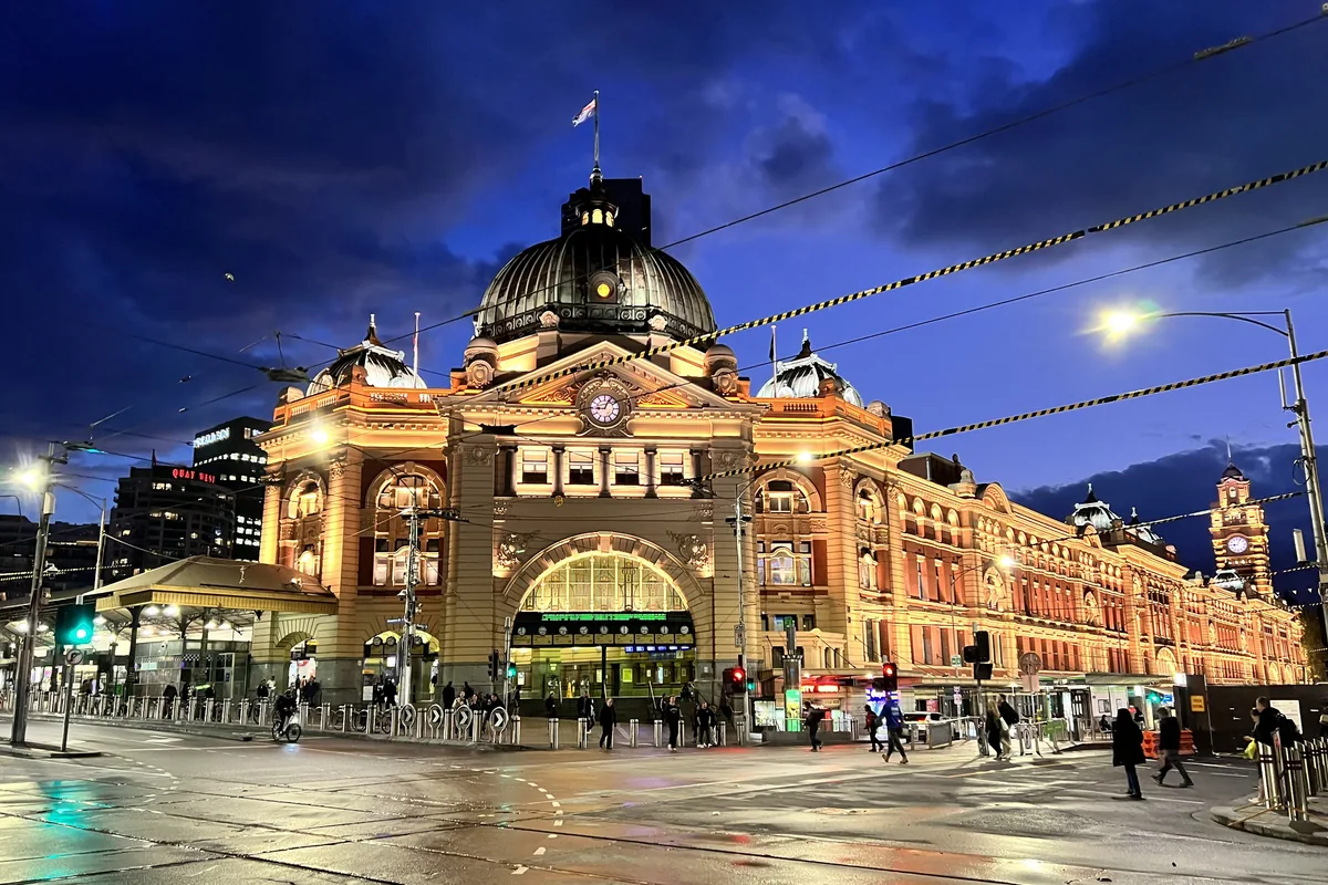 La gare de Flinders Street de nuit, son bâtiment édouardien à coupole illuminé d'or sur un ciel bleu profond.