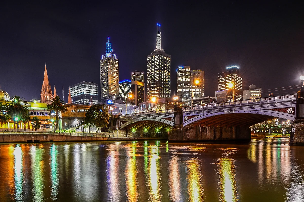 Le pont Princes s'arqua au-dessus de la Yarra à la nuit tombée, avec les tours de la ville en arrière-plan et des reflets colorés dans l'eau.