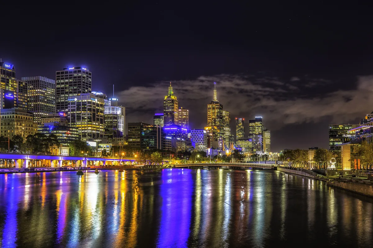Le Yarra de nuit, avec les lumières de la ville en arrière-plan et leurs reflets bleu vif, dorés et blancs sur l'eau sombre.